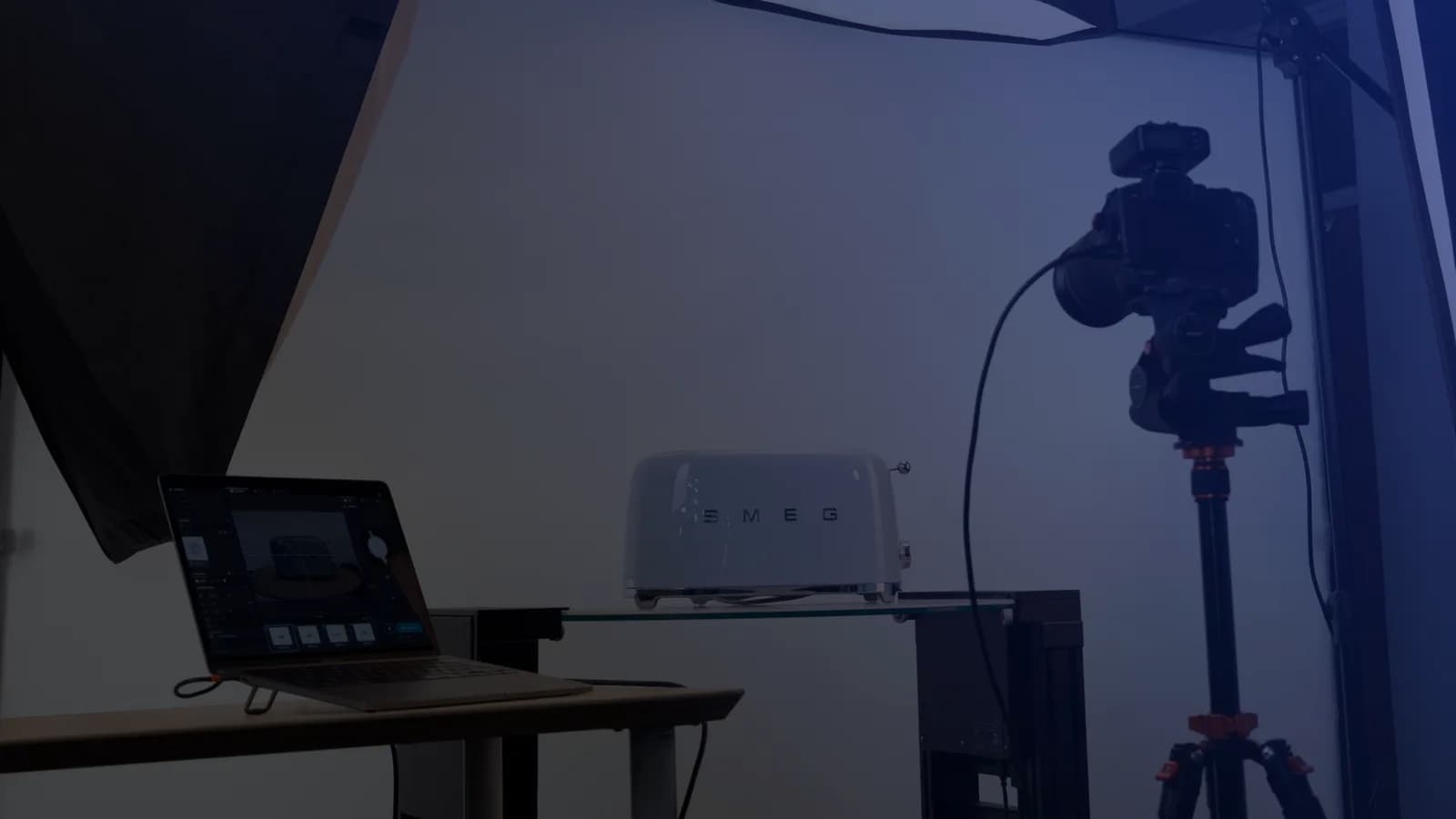 Set de fotografia de produto com tethering: um notebook com o software de captura ao lado de uma câmera no tripé e um produto sobre uma prateleira de vidro