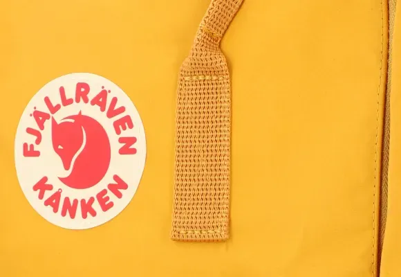 Close-up do logo e da alça da mochila Kanken amarela