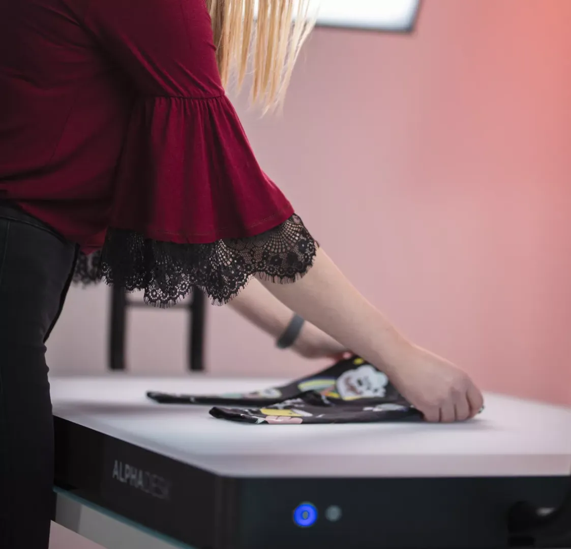 Mulher dobrando roupas infantis em uma mesa branca com Alphadesk
